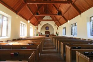 Leerer Kirchenraum mit Holzbankreihen, Mittelgang und farbigen Fenstern