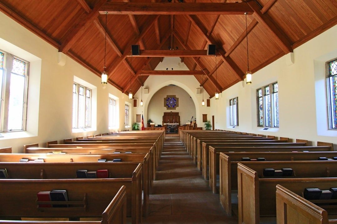 Leerer Kirchenraum mit Holzbankreihen, Mittelgang und farbigen Fenstern